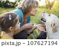 Gray-haired grandmother and cute little granddaughter are walking their dogs together in the park. 107627194