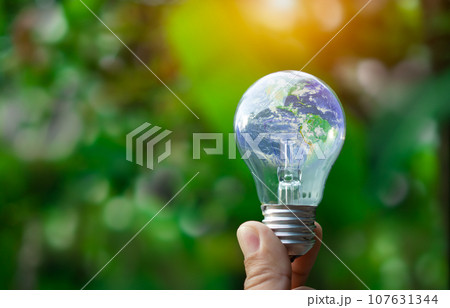 Concept of renewable energy, environmental protection, and sustainable renewable energy sources. World map on a light bulb set on a background nature green. Green energy. 107631344