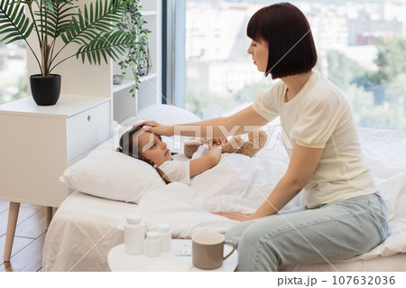 Caring mother checking temperature with hand of sick child 107632036