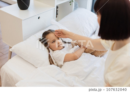 Mother touching forehead of her sick little daughter in bed Mother touching forehead of her sick little daughter in bed 107632040