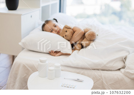 Little girl with virus resting on comfy bed with toy bear 107632200