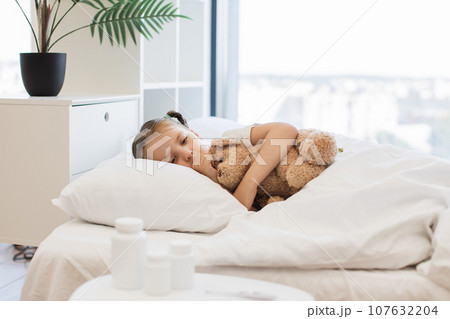 Fatigued cute girl hugging toy bear and coughing in bed 107632204
