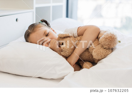 Fatigued cute girl hugging toy bear and coughing in bed 107632205