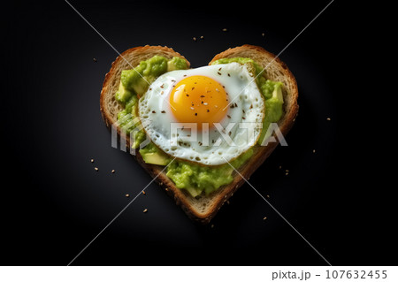 One sandwich in shape of heart spread with avocado paste with fried egg isolated on black background flat lay. Generative AI One sandwich in shape of heart spread with avocado paste with fried egg isolated on black background flat lay. Generative AI 107632455