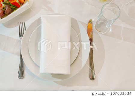 White round plate with serving napkin on table. White round plate with serving napkin on table. 107633534