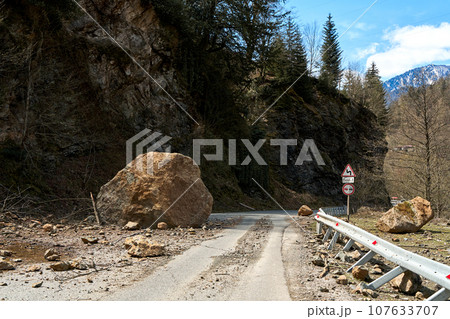 A huge rock fell from the mountains onto the road, destroying the asphalt and blocking half of the roadway A huge rock fell from the mountains onto the road, destroying the asphalt and blocking half of the roadway 107633707