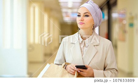 Muslim businesswoman walks scrolling social media on phone 107633809