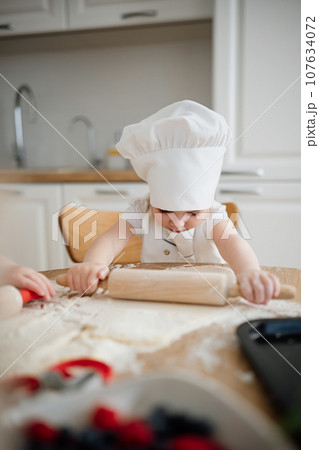 Funny girl in chef hat and apron rolling out pastry dough 107634072