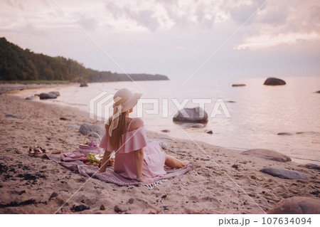 Young woman in straw hat sit on plaid have picnic on sea sunrise sand beach Young woman in straw hat sit on plaid have picnic on sea sunrise sand beach 107634094
