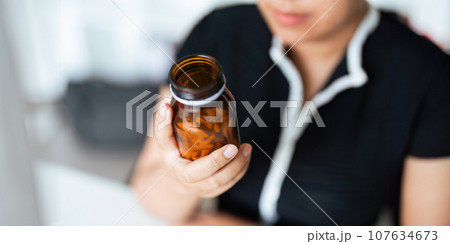 Woman hold bottle of drug tablet painkiller or vitamin supplement reading label ready to organizing medicine at home. medication healthcare concept 107634673
