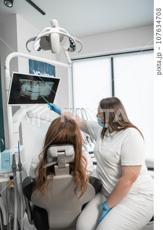 The dentist examines the results of a CT scan of the patient's mouth for an accurate diagnosis. Patients can expect the highest standard of dental care in a modern medical center. 107634708
