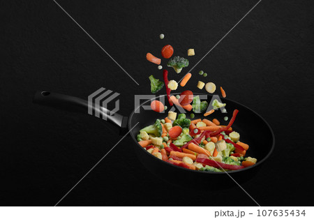 Falling frozen vegetables in a frying pan on black background. Vegetable mix flying down. Healthy natural food. 107635434