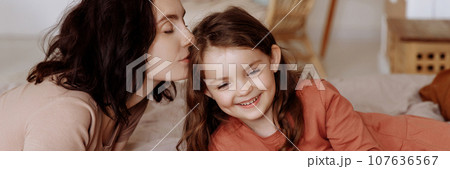Happy cute little girl with a beautiful young mother lie on the bed 107636567