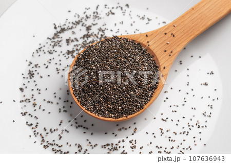 Healthy raw chia seeds in a wooden spoon on white ceramic surface close up Healthy raw chia seeds in a wooden spoon on white ceramic surface close up 107636943