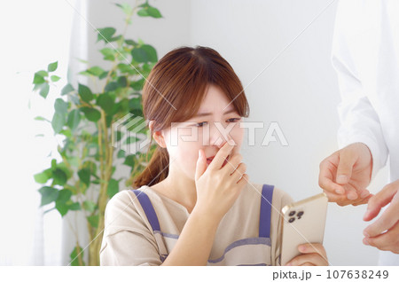 男性のスマホを見て複雑な表情をする女性 107638249