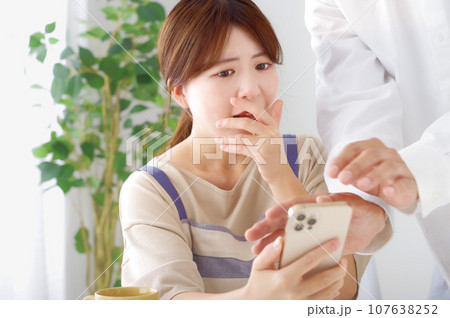 男性のスマホを見て複雑な表情をする女性 男性のスマホを見て複雑な表情をする女性 107638252