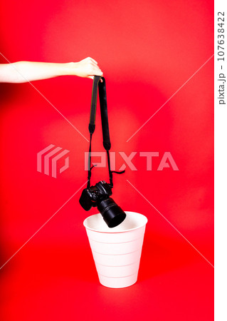 Hand with old digital camera in a trash can, isolated on a red background 107638422