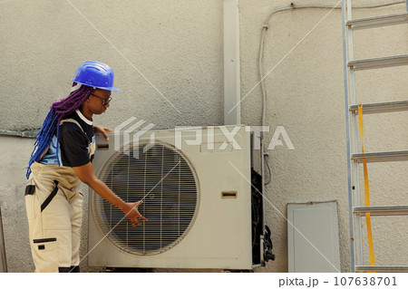 Trained worker dissasembling air conditioner outer front grill in order to start servicing broken internal parts. Knowleadgeable engineer comissioned by home owner to do maintenance on hvac system 107638701