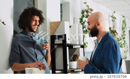 Colleagues relaxing on coffee break, having conversation and enjoying laugh together. Two business partners talking to each other before starting to work on startup development. Colleagues relaxing on coffee break, having conversation and enjoying laugh together. Two business partners talking to each other before starting to work on startup development. 107638706