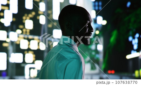 Happy entrepreneur on night walk enjoying town landscapes with street lights, feeling relaxed on late promenade. Businessman strolling around city center business district. Handheld shot. 107638770