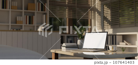 A white-screen laptop mockup on a coffee table in a modern living room. Home workspace 107641403