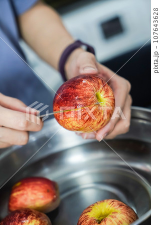 woman hand is cleaning red apple in bucket of water, closed up shot 107643628