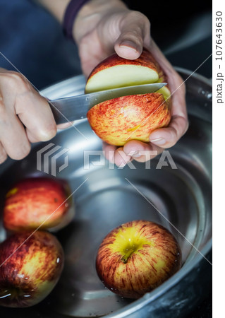 woman hand is cleaning red apple in bucket of water, closed up shot woman hand is cleaning red apple in bucket of water, closed up shot 107643630