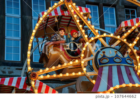 Little preschool girl and school boy riding on ferris wheel carousel horse at Christmas funfair or market, outdoors. Two happy children having fun on traditional family xmas market in Germany Little preschool girl and school boy riding on ferris wheel carousel horse at Christmas funfair or market, outdoors. Two happy children having fun on traditional family xmas market in Germany 107644662