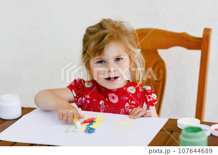 Little creative toddler girl painting with finger colors a fish. Active child having fun with drawing at home, in kindergaten or preschool. Education and distance learning for kids. Creaitve activity. 107644689