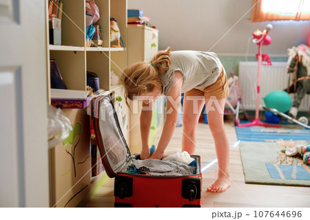 Little girl packing suitcase at home. Cute child putting clothes into suitcase. Preparing for family vacations with children. Practicing independence Little girl packing suitcase at home. Cute child putting clothes into suitcase. Preparing for family vacations with children. Practicing independence 107644696