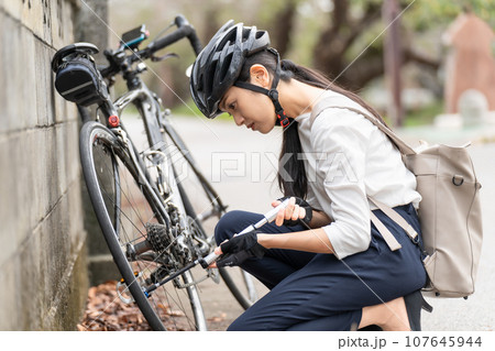 ロードバイクに 携帯用ポンプで空気を入れている若い女性 107645944