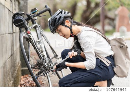 ロードバイクに 携帯用ポンプで空気を入れている若い女性 ロードバイクに 携帯用ポンプで空気を入れている若い女性 107645945