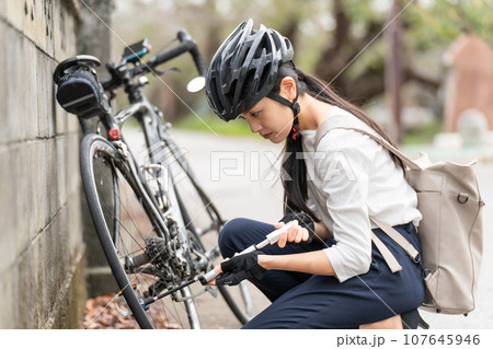 ロードバイクに 携帯用ポンプで空気を入れている若い女性 ロードバイクに 携帯用ポンプで空気を入れている若い女性 107645946