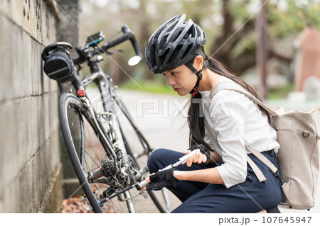 ロードバイクに 携帯用ポンプで空気を入れている若い女性 107645947