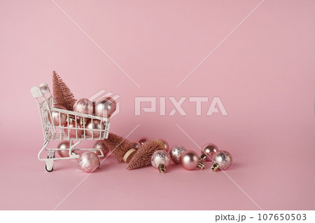 White shopping cart with Christmas decorations on pink background with copy space. Christmas shopping concept White shopping cart with Christmas decorations on pink background with copy space. Christmas shopping concept 107650503