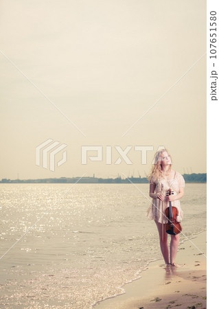 Woman on beach near sea holding violin Woman on beach near sea holding violin 107651580