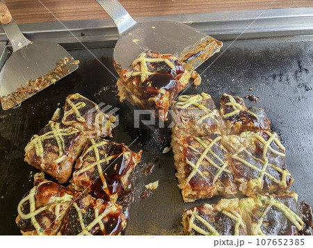鉄板で焼いてるお好み焼き取り分ける 鉄板で焼いてるお好み焼き取り分ける 107652385