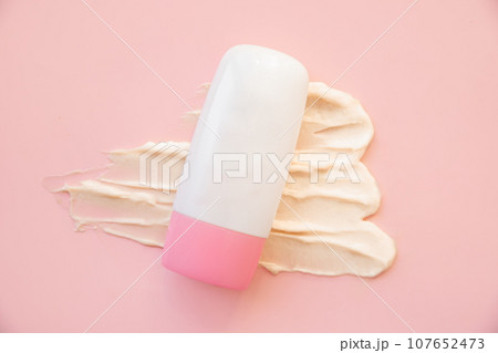 cosmetic moisturizing cream in tube bottle with pink screw cap and ivory color smear of moisturizer on pink background. Skin care, sunscreen container, lotion, balsam, hand creme or packaging mockup. 107652473