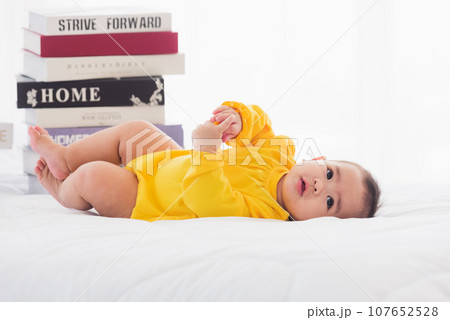 Asian cute baby little girl toddler looking at a stack of books on bedroom white bed, First baby library concept Asian cute baby little girl toddler looking at a stack of books on bedroom white bed, First baby library concept 107652528