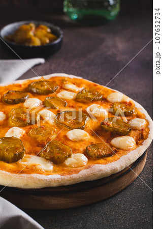 Pizza with pickles and mozzarella on a wooden board on the table vertical view Pizza with pickles and mozzarella on a wooden board on the table vertical view 107652734
