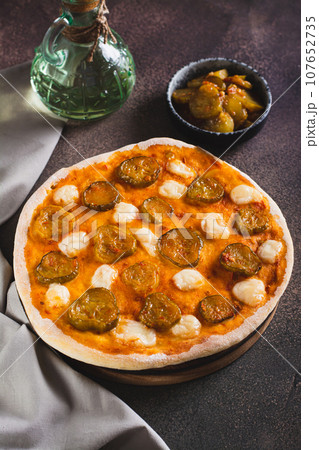 Spicy pizza with cheese and pickles on a wooden board on the table vertical view 107652735