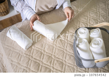 Housewife woman folding roll towels for comfortable storage in metallic basket bedroom tidying up Housewife woman folding roll towels for comfortable storage in metallic basket bedroom tidying up 107654542