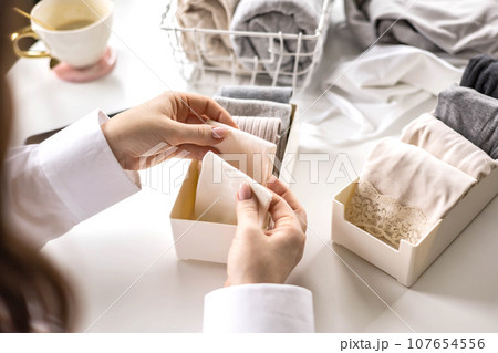 Housewife woman hands folded cotton linen domestic textile in box container and basket on table desk Housewife woman hands folded cotton linen domestic textile in box container and basket on table desk 107654556