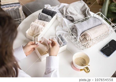 Housewife woman hands folded cotton linen domestic textile in box container and basket on table desk Housewife woman hands folded cotton linen domestic textile in box container and basket on table desk 107654558