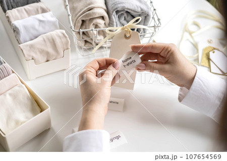Woman hands cutting sticker tag scissors comfortable storage organizing linen textile in container Woman hands cutting sticker tag scissors comfortable storage organizing linen textile in container 107654569