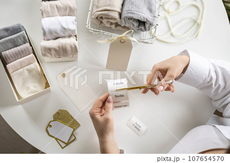 Woman hands cutting sticker tag scissors comfortable storage organizing linen textile in container Woman hands cutting sticker tag scissors comfortable storage organizing linen textile in container 107654570