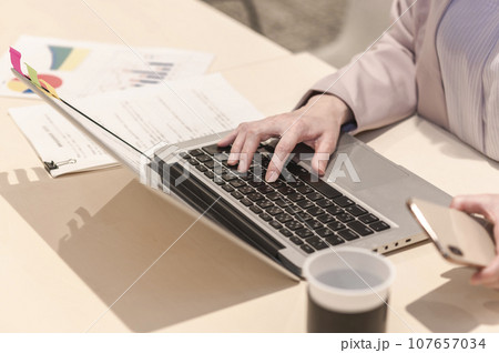 スマホを持ちながらノートパソコンをタイピングする女性 107657034