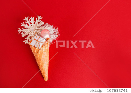 Ice Cream Cone with Christmas Decoration snowflake and gift box on red background Ice Cream Cone with Christmas Decoration snowflake and gift box on red background 107658741