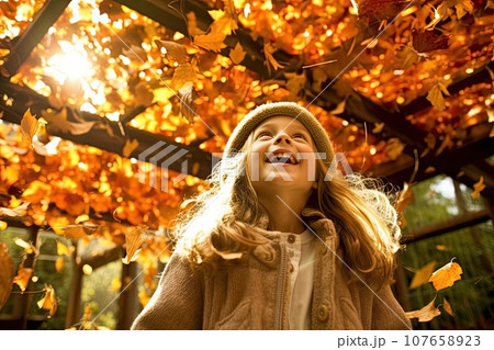 a little girl playing with autumn leaves in the park, she is laughing and looking up to the sky stock photo 107658923