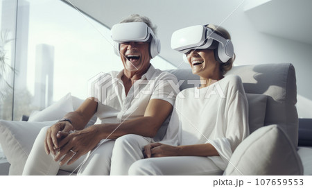 Senior mature couple wearing virtual reality headsets sits on the sofa having fun together. Happy retired people using modern VR goggle glasses. New trends and technology concept for all ages. 107659553